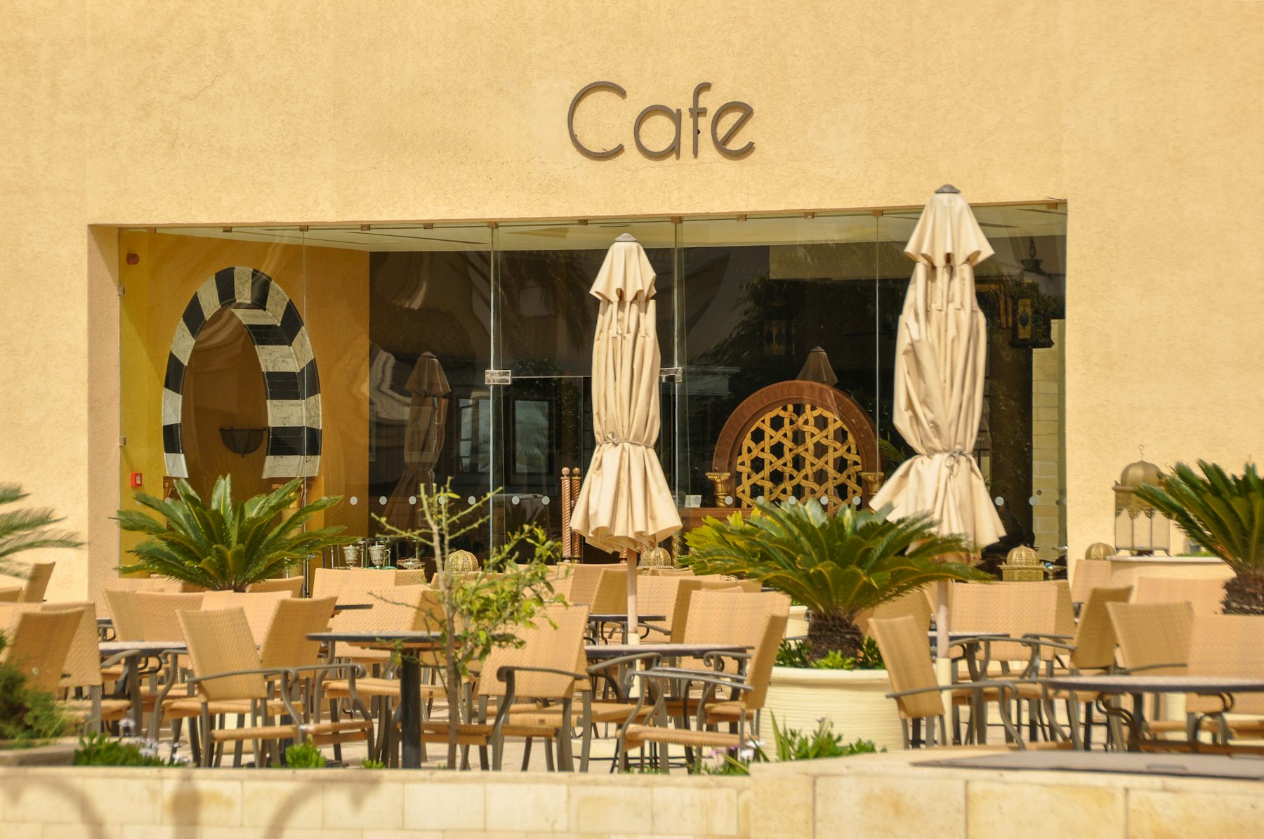 Fachada de una cafetería con terraza y sombrillas al sol