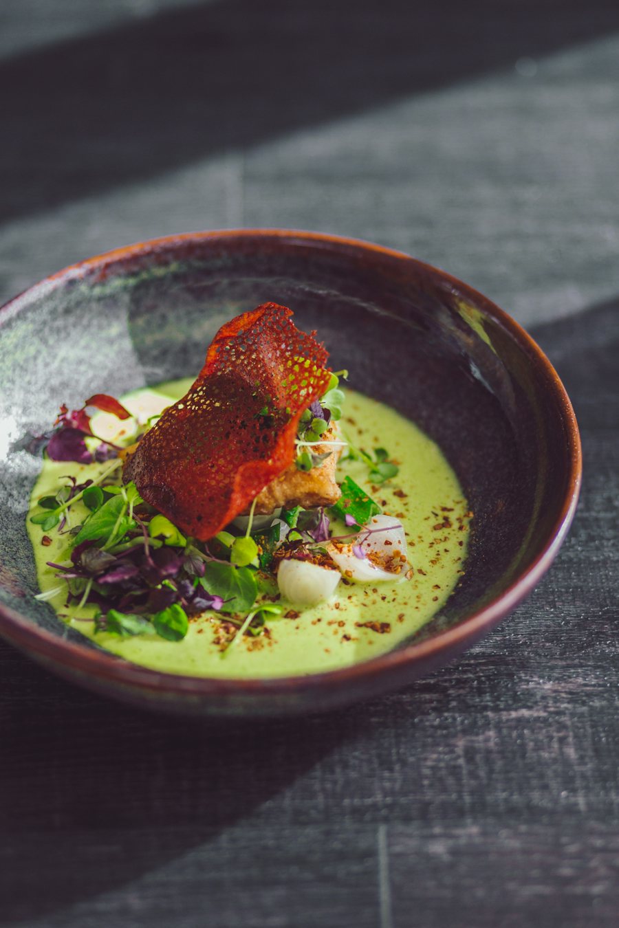 Plato de autor con carne glaseada sobre una crema verde